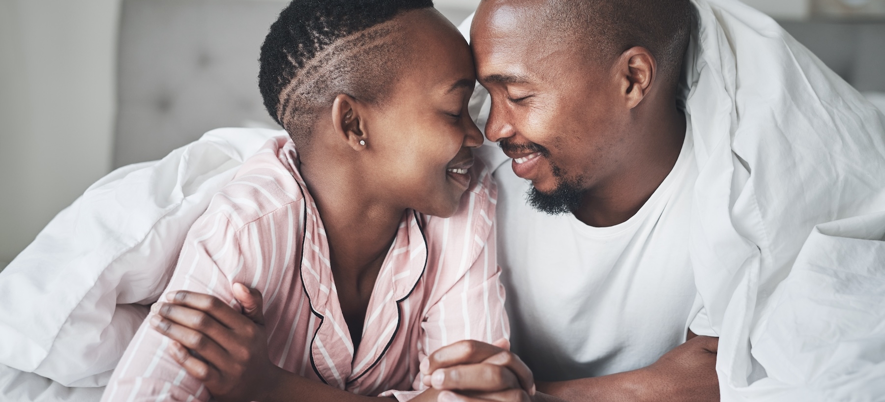 Love, relax and black couple lying in bed in a hotel for valentines day, anniversary or romance. Intimacy, happy and young African man and woman relaxing in bedroom while on romantic vacation or trip.