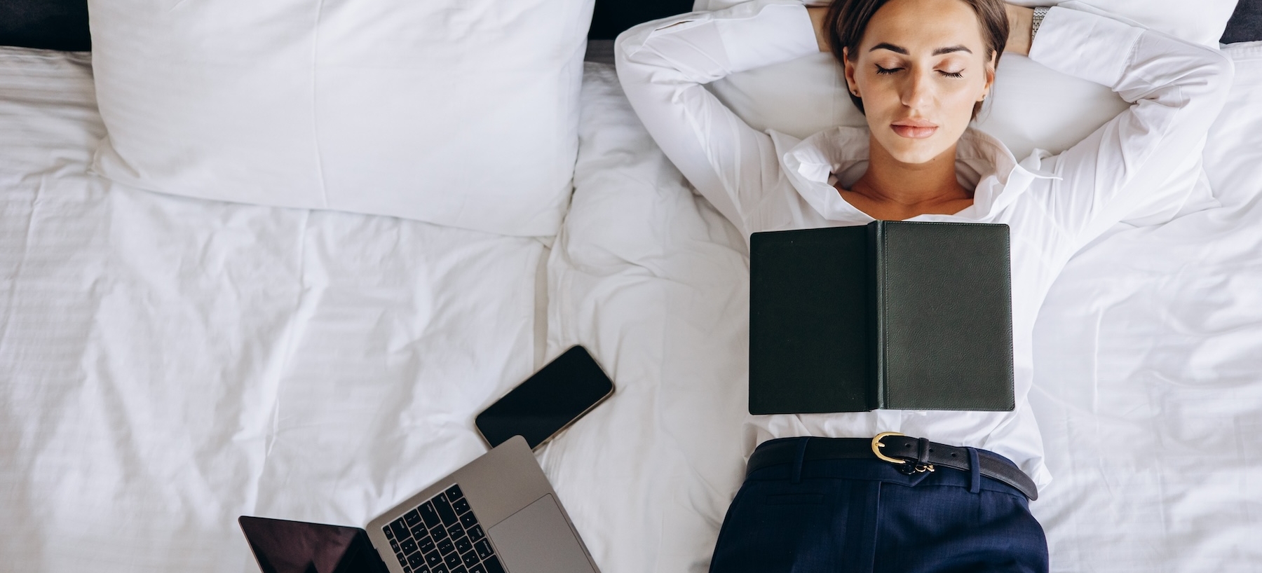 Business woman sleeping in a hotel room with laptop and phone lying on bed